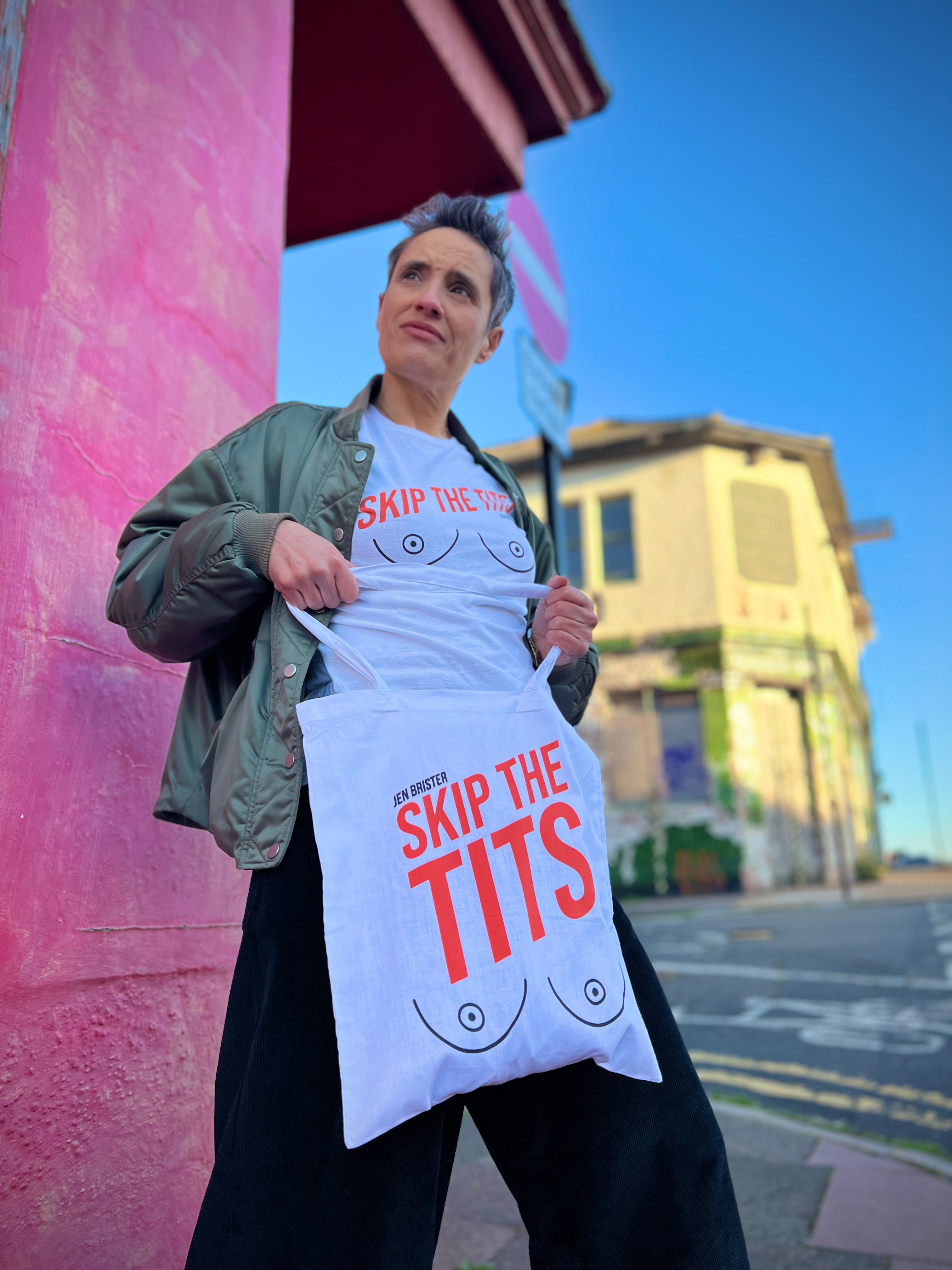 Person holding a tote bag with 'Skip the Tits' text against a pink wall.