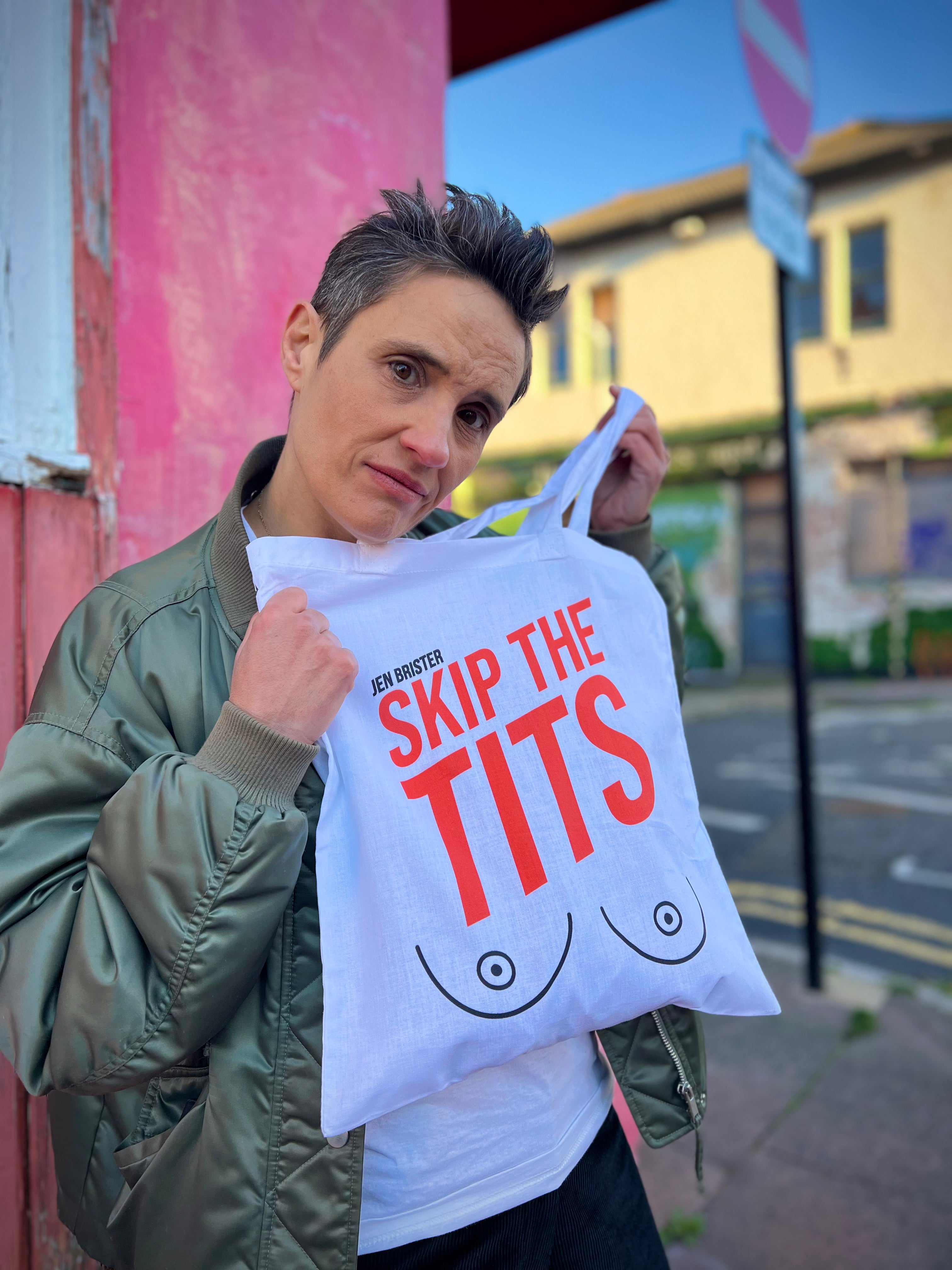 Person holding a tote bag with 'SKIP THE TITS' text outdoors.